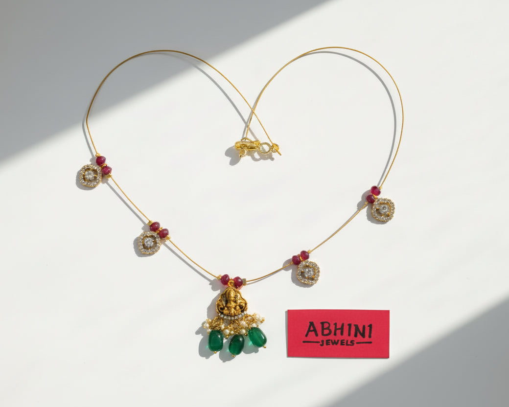 Gold necklace with red and green beads on a pink and white background with 'ABHINI JEWELS' label.
