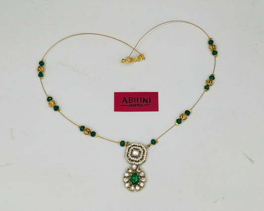 Necklace with green and gold beads and a pendant on a pink and white background, featuring the brand 'ABHINI'.