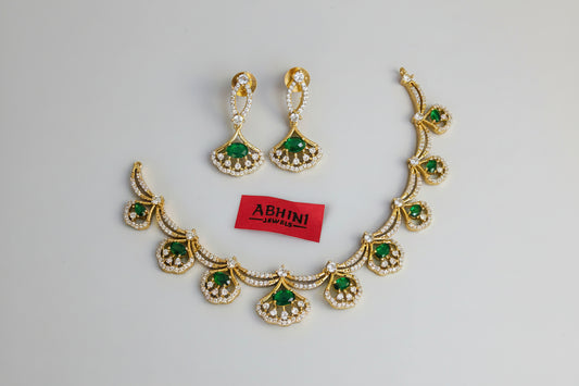 Gold necklace with green stones and matching earrings on a gray background, branded 'Abhini'.